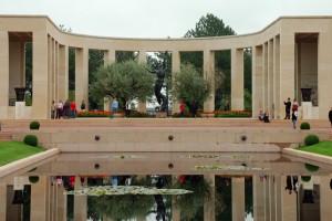The semi-circular colonnade and bronze statue are reflected in a still pool at the American cemetery in Colleville-sur-Mer