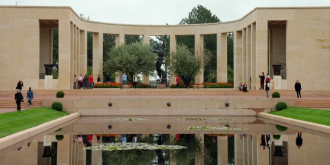 The semi-circular colonnade and bronze statue are reflected in a still pool at the American cemetery in Colleville-sur-Mer